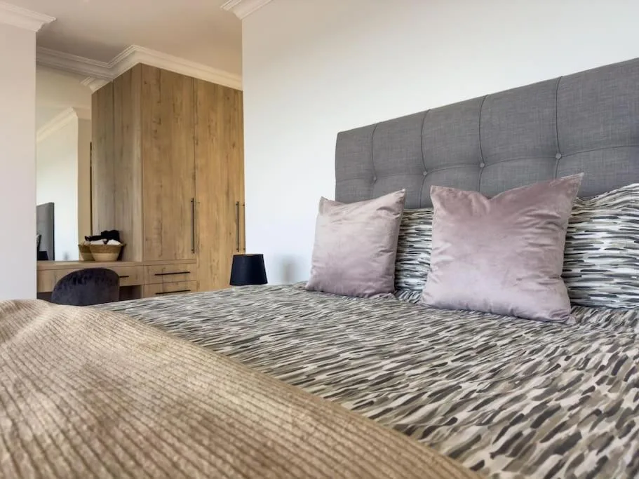 Modern bedroom with upholstered gray headboard, patterned bedding, and wooden wardrobe