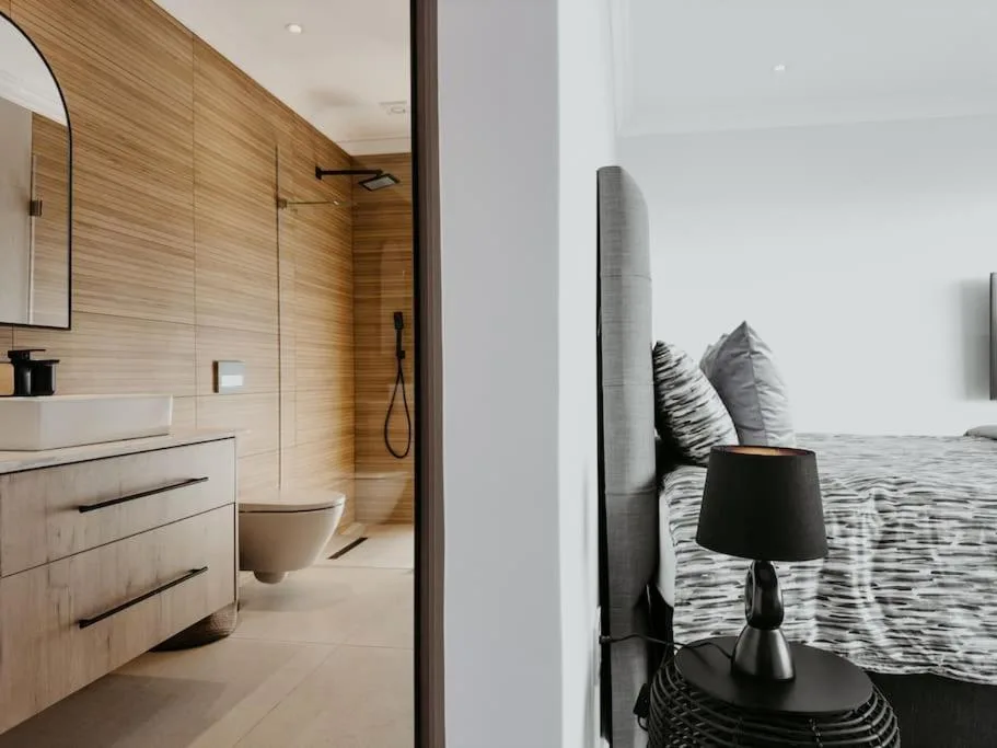 Modern bedroom with en-suite bathroom featuring wooden vanity and rainfall shower