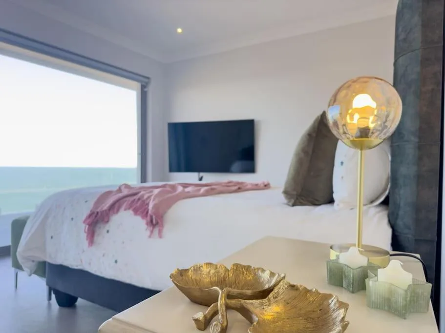 Modern bedroom with ocean view, wall-mounted TV, and contemporary gold lamp decor