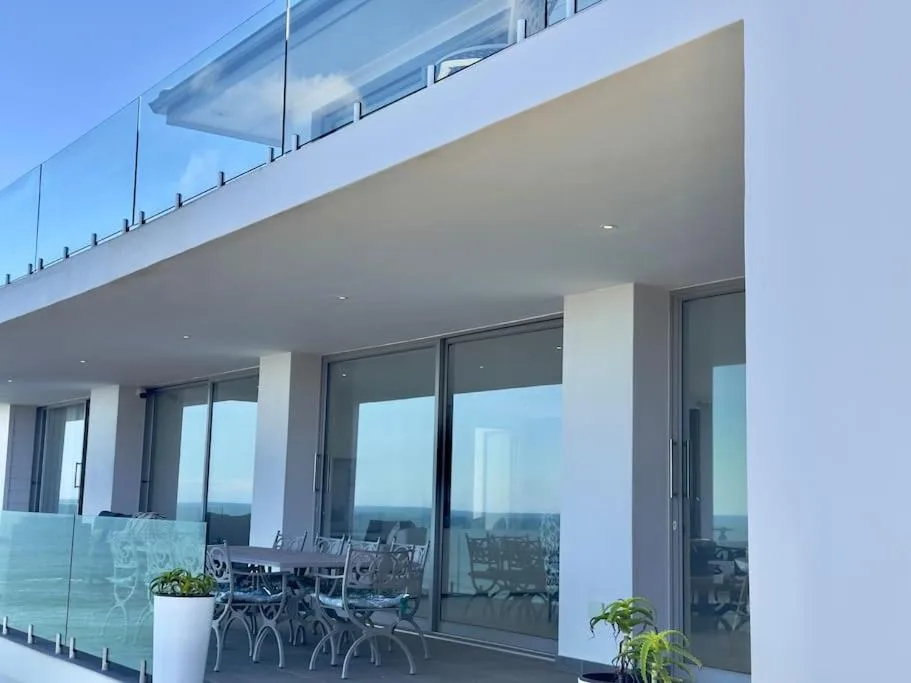 Modern covered deck with dining chairs and panoramic glass railings overlooking landscape