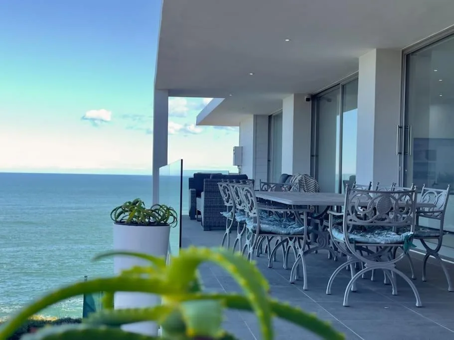 Oceanfront deck with dining table, chairs, and panoramic sea views
