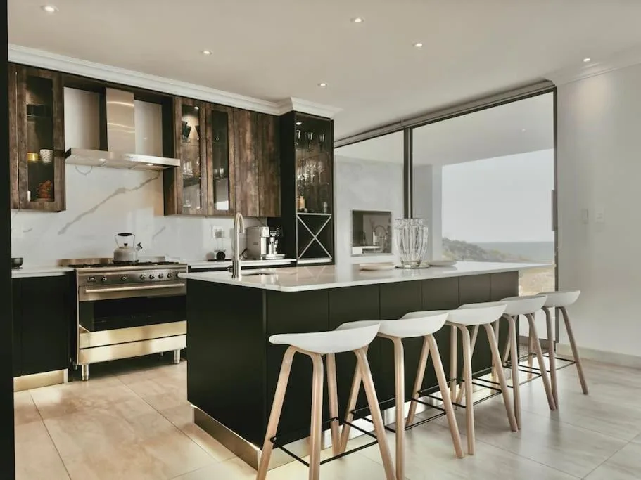 Modern kitchen with black cabinetry, island seating, and ocean views through sliding doors