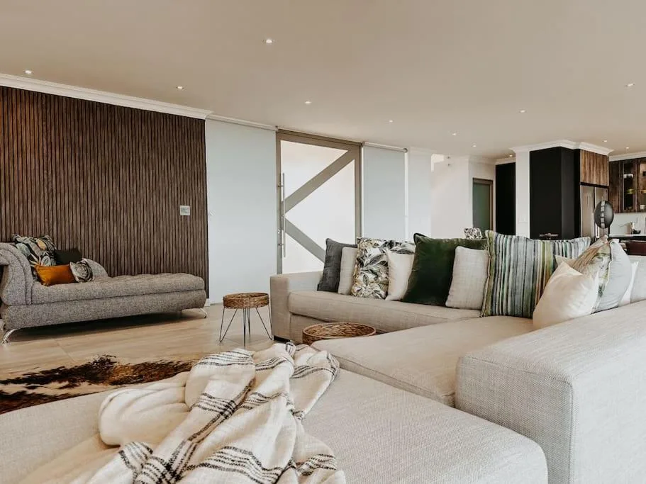 Modern open-plan lounge with cream sofas, decorative pillows, and contemporary furnishings
