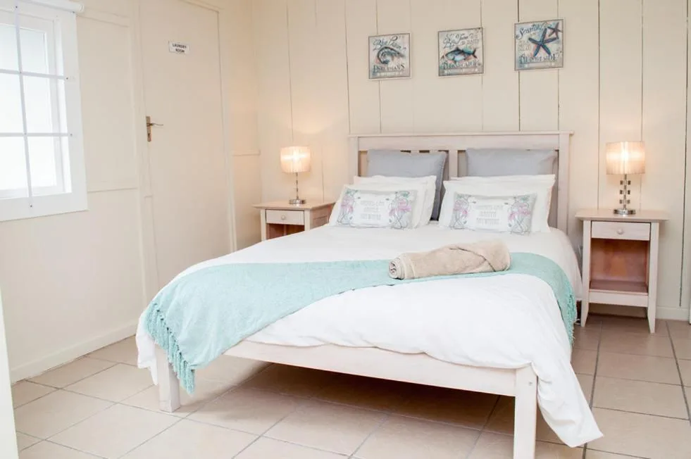 Bright bedroom with white bed, turquoise throw, and coastal wall art