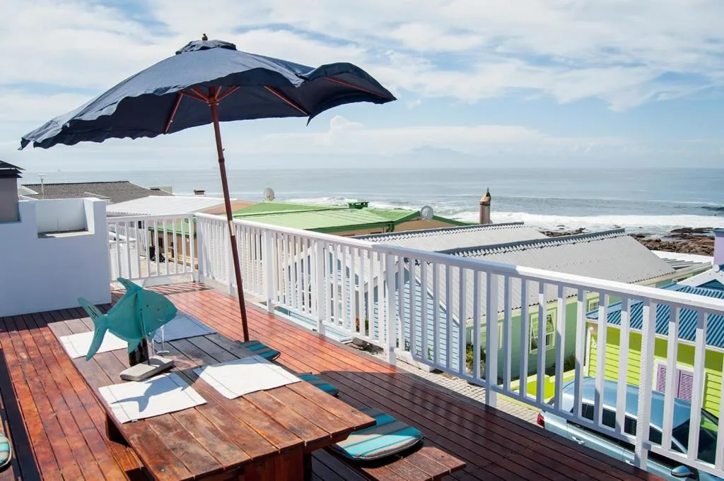 Oceanfront deck with umbrella, loungers, and white railings overlooking beach