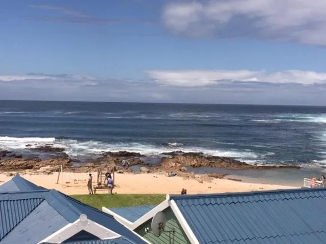 Ocean view with sandy beach, rocky shoreline, and blue sky from property
