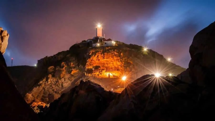 Cape Point lighthouse illuminated at twilight with rocky coastline below