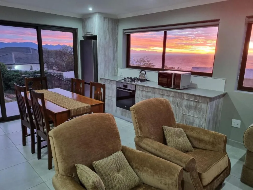 Open-plan lounge with upholstered armchairs overlooking mountain sunset views through large windows