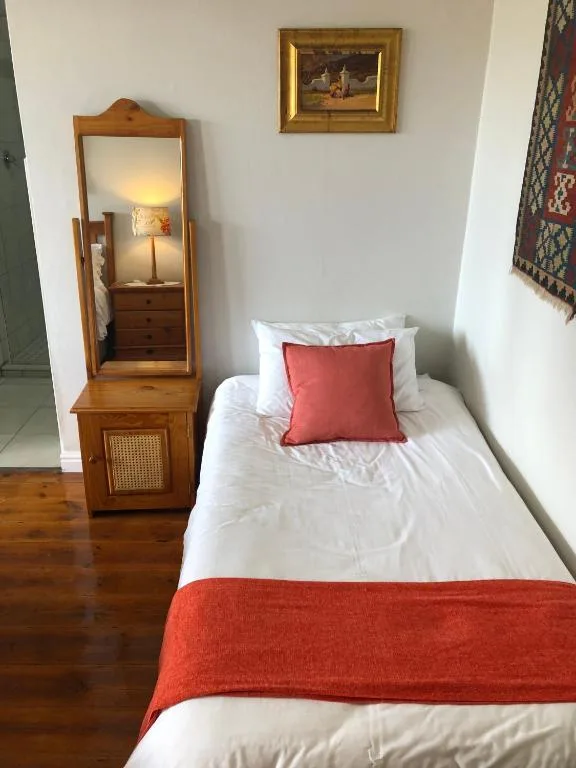 Single bed with white linens and red accents, wooden mirror and decor