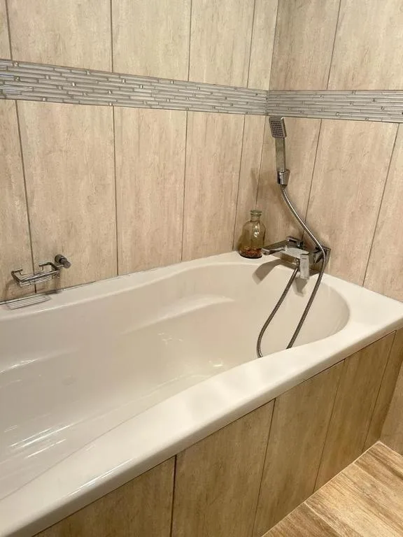 Modern white bathtub with hand shower and wood-paneled walls
