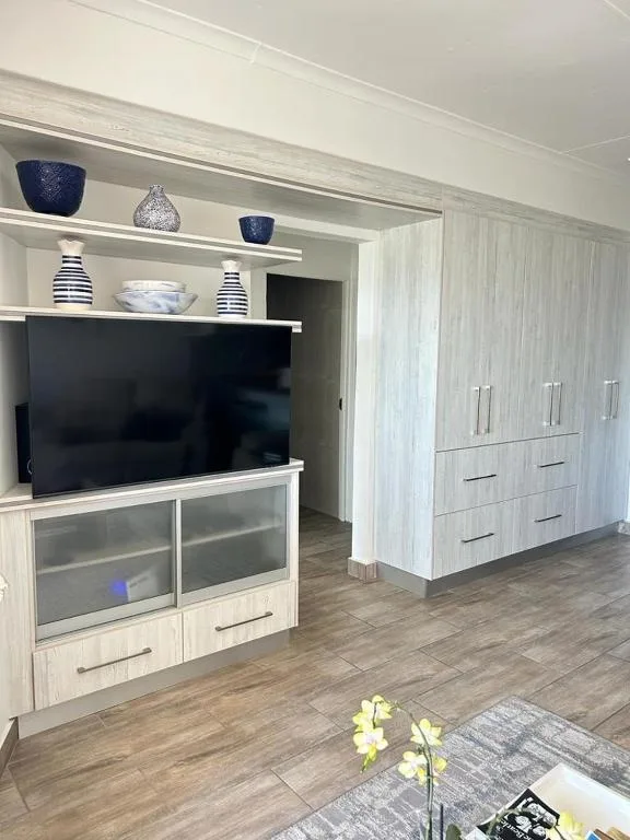 Modern lounge with flat-screen TV, built-in shelving, and light wood cabinetry