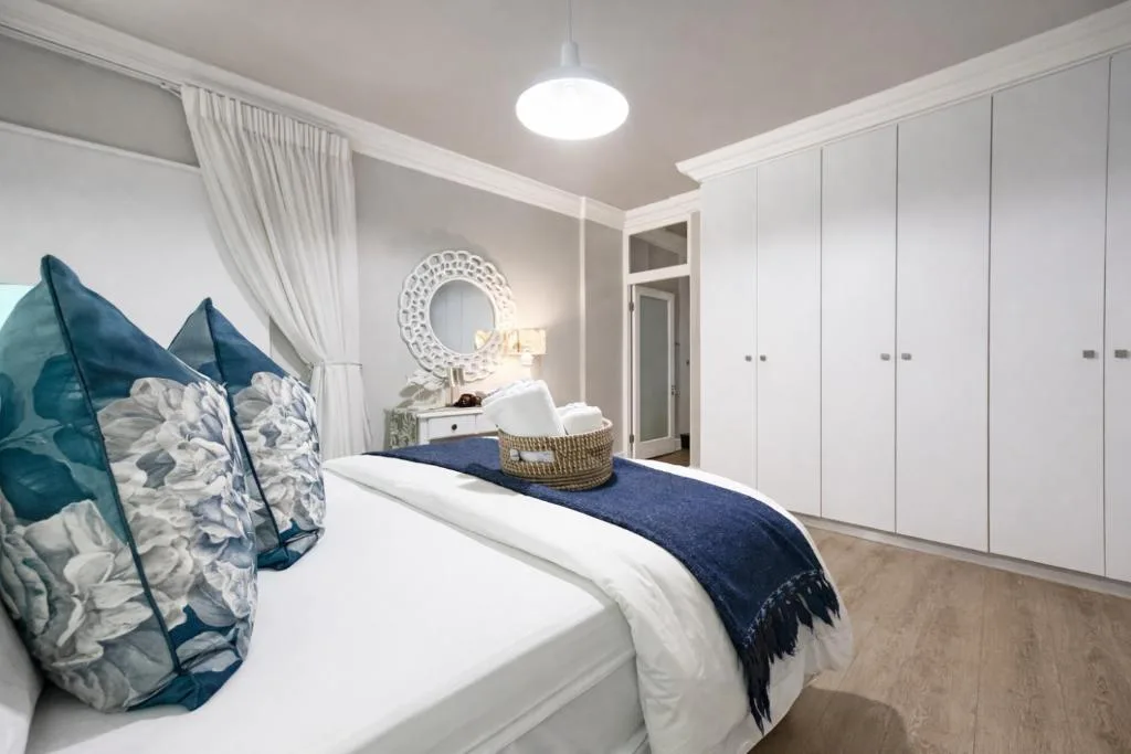 Bright bedroom with queen bed, teal pillows, white built-in wardrobes, pendant lighting
