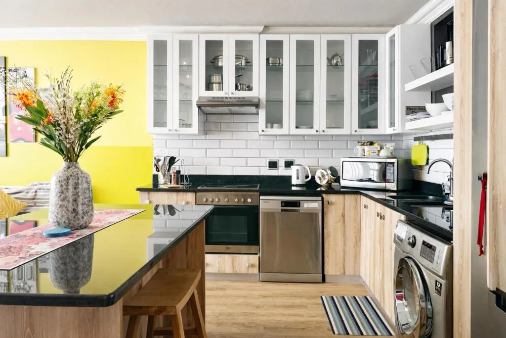 Modern kitchen with yellow accent wall, white cabinetry, black countertops, and stainless steel appliances