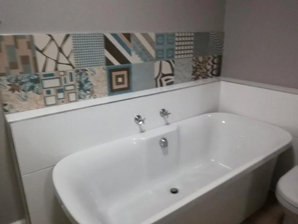 Modern white freestanding bathtub with chrome fixtures and patterned tile backsplash