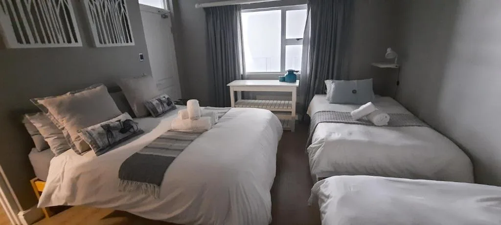 Modern bedroom with multiple beds, grey curtains, and natural light from windows