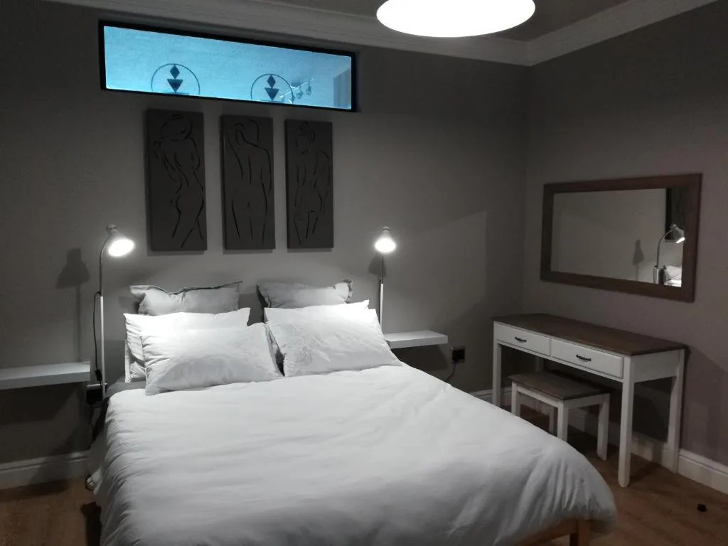 Modern bedroom with white bedding, vanity desk, and abstract wall art