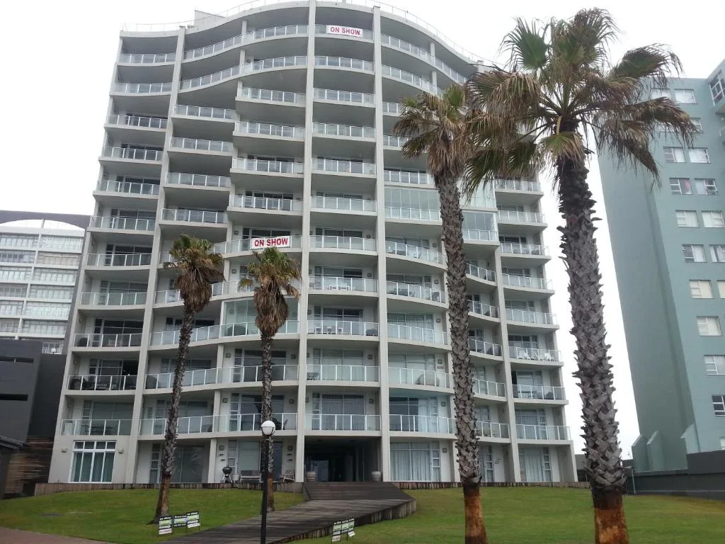 Modern multi-story apartment building with palm trees and green lawn
