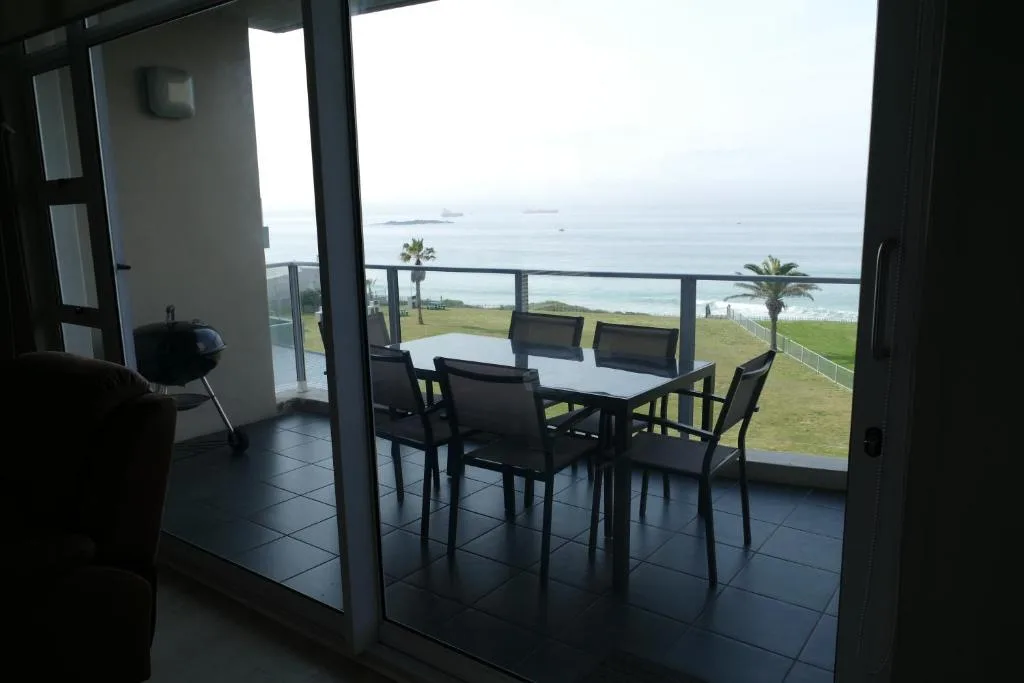 Oceanview deck with dining table, chairs, and lagoon beyond green lawn
