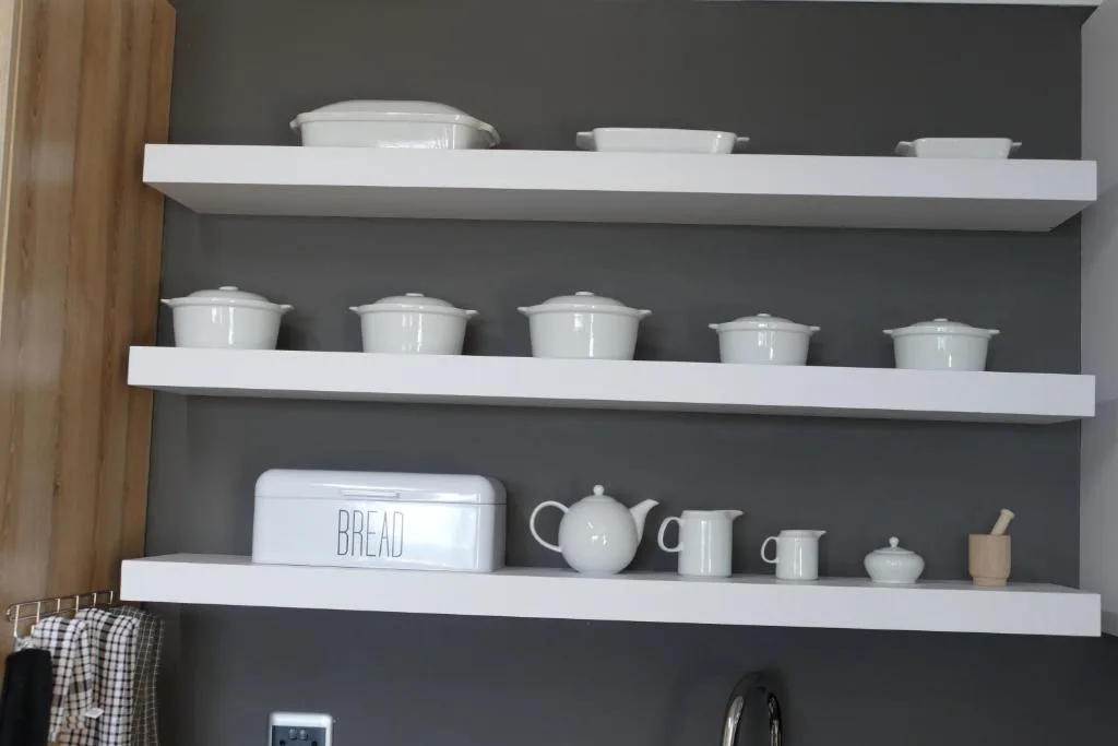 Kitchen shelving with white dishware, bread box, and teapot collection