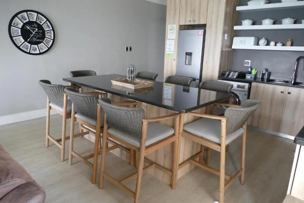 Modern dining table with six woven chairs and open-plan kitchen beyond