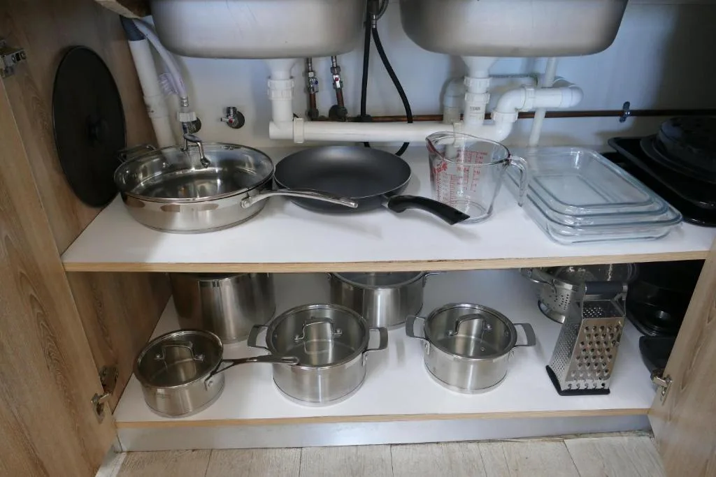Under-sink storage with stainless steel cookware and kitchen utensils organized on shelves