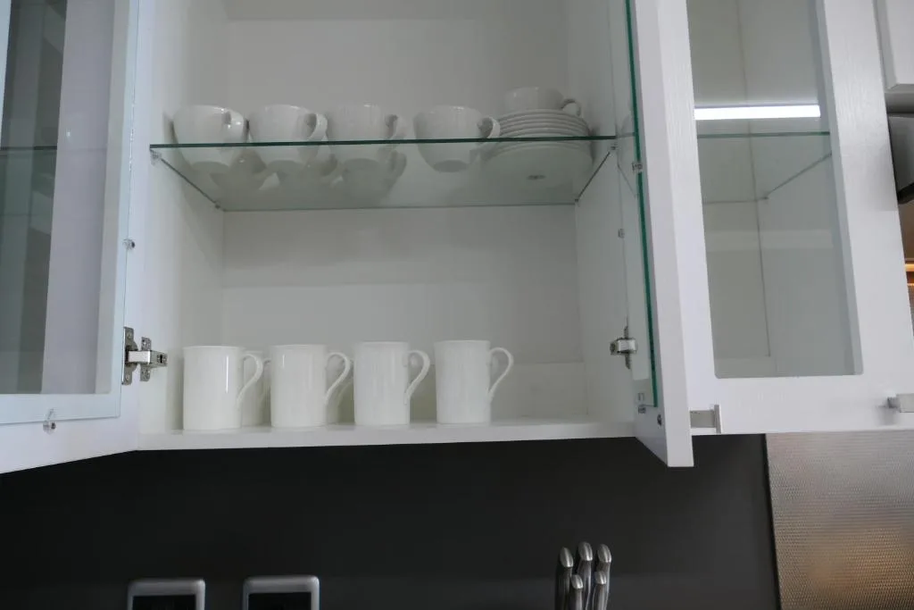 Open white kitchen cabinet displaying white mugs and stacked plates