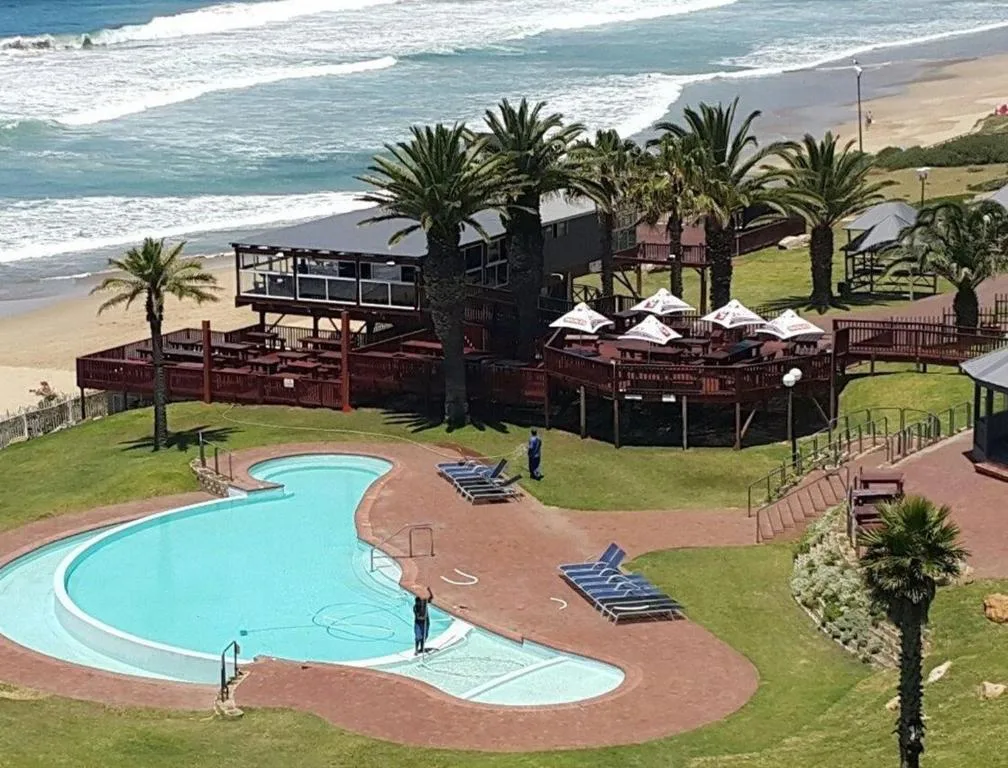 Curved swimming pool with beach and ocean waves beyond palm trees