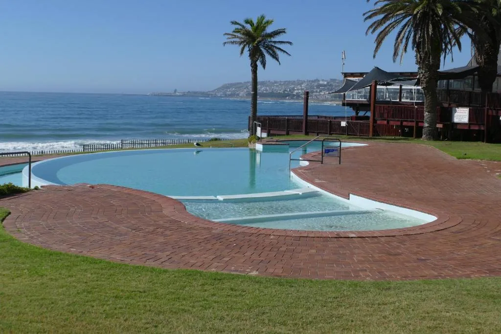 Curved swimming pool overlooking ocean beach with palm trees and coastal town