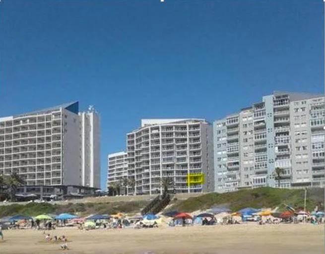 Beach frontage with sandy shore, colorful umbrellas, beachgoers, apartment buildings