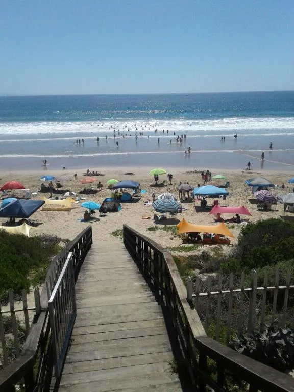 Scenic beach view with ocean, sand, and swimmers from wooden boardwalk