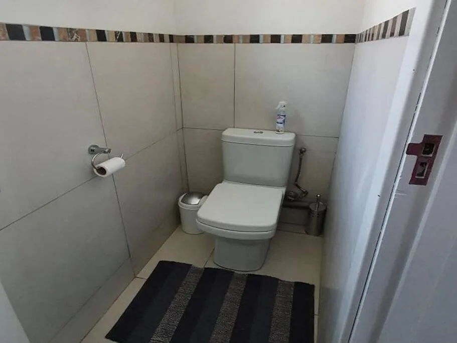Clean bathroom with white toilet, neutral tiled walls, and striped floor mat