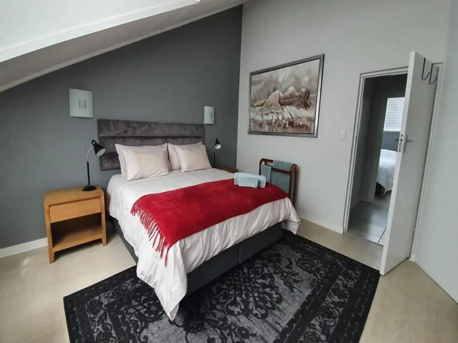 Bedroom with queen bed, red throw, wooden nightstand, and artwork