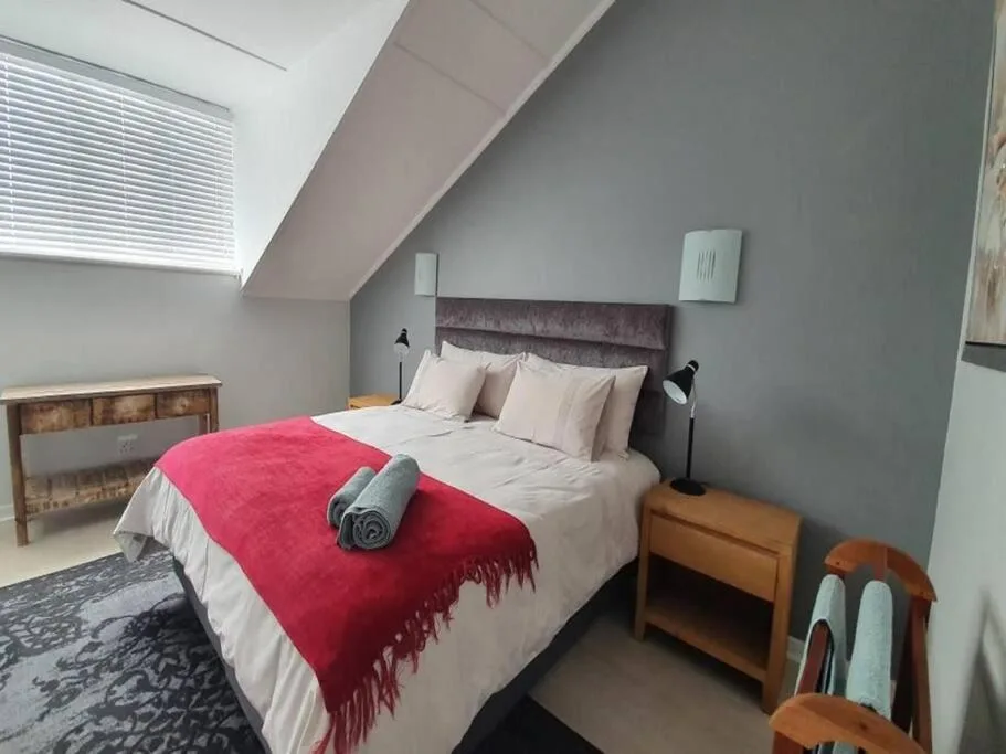 Cozy attic bedroom with double bed, red throw blanket, and wooden nightstands