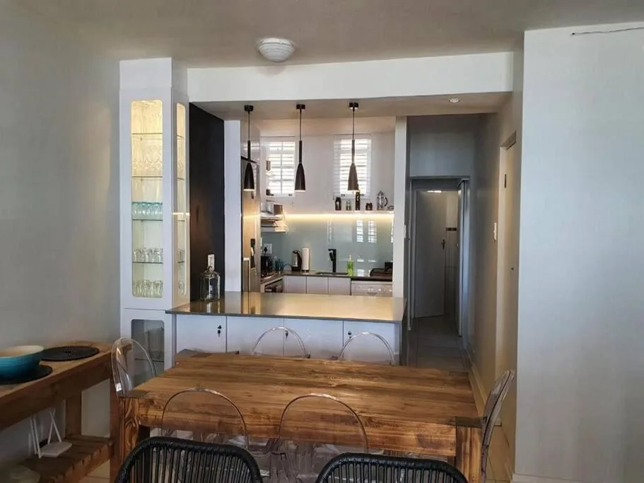 Wooden dining table with woven chairs, kitchen visible through open counter pass-through