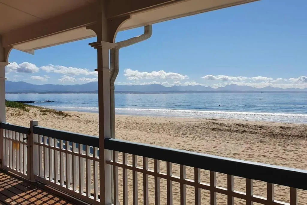 Beachfront vista with sandy shore, ocean, and mountains from covered deck