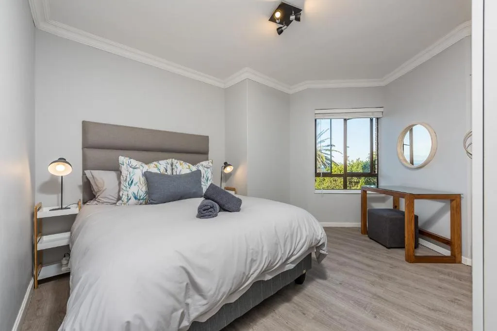 Bright modern bedroom with queen bed, gray headboard, and garden views