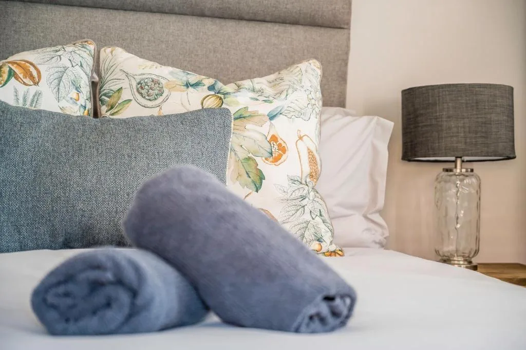 Neatly made bed with rolled towels and botanical patterned pillows