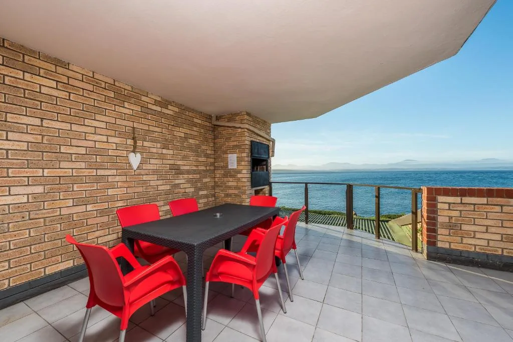 Oceanfront deck with red chairs, dining table, and sea view