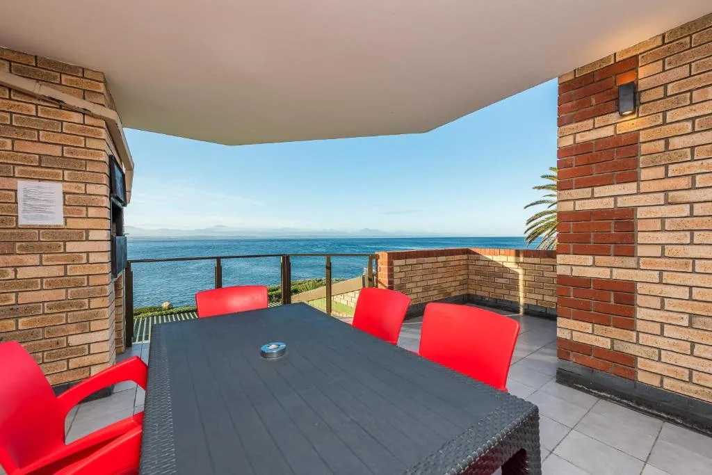 Outdoor deck with red chairs and table overlooking ocean and mountains