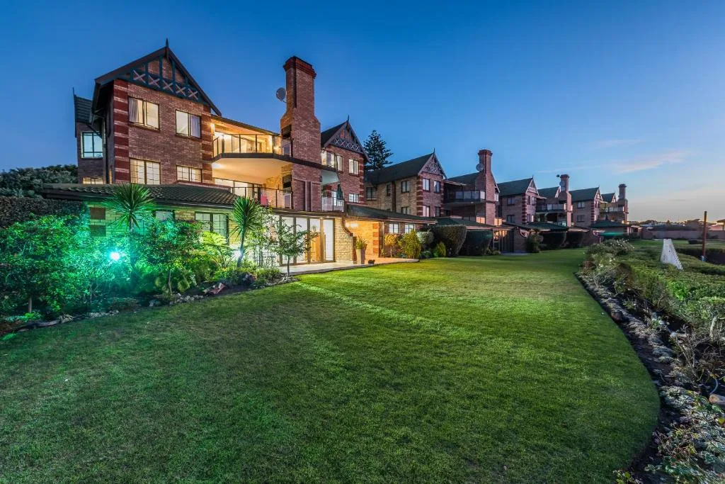 Illuminated Victorian-style brick building with manicured lawn and neighboring properties at dusk