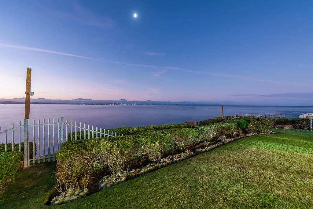 Expansive lagoon and mountain vista from manicured garden with fencing