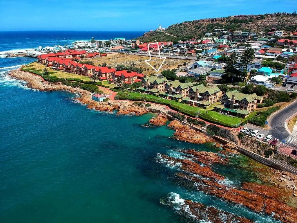 Aerial view of coastal town with turquoise ocean, red rocky cliffs, and beachfront properties