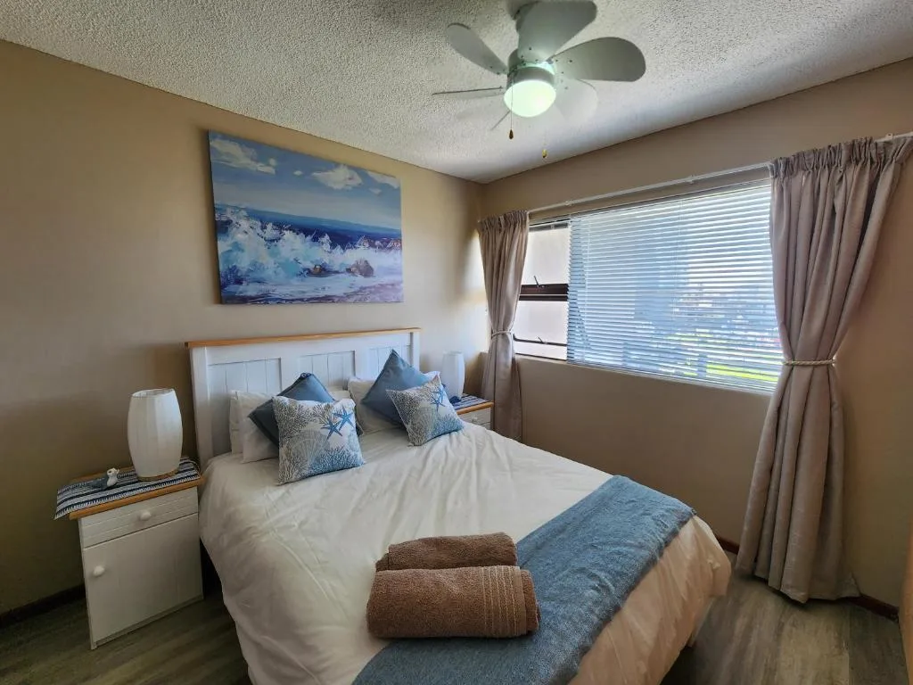 Bright bedroom with queen bed, blue accents, ceiling fan, and large window
