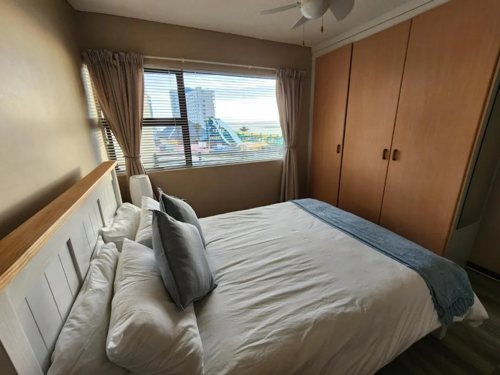 Bright bedroom with queen bed, large window overlooking coastal town and sea