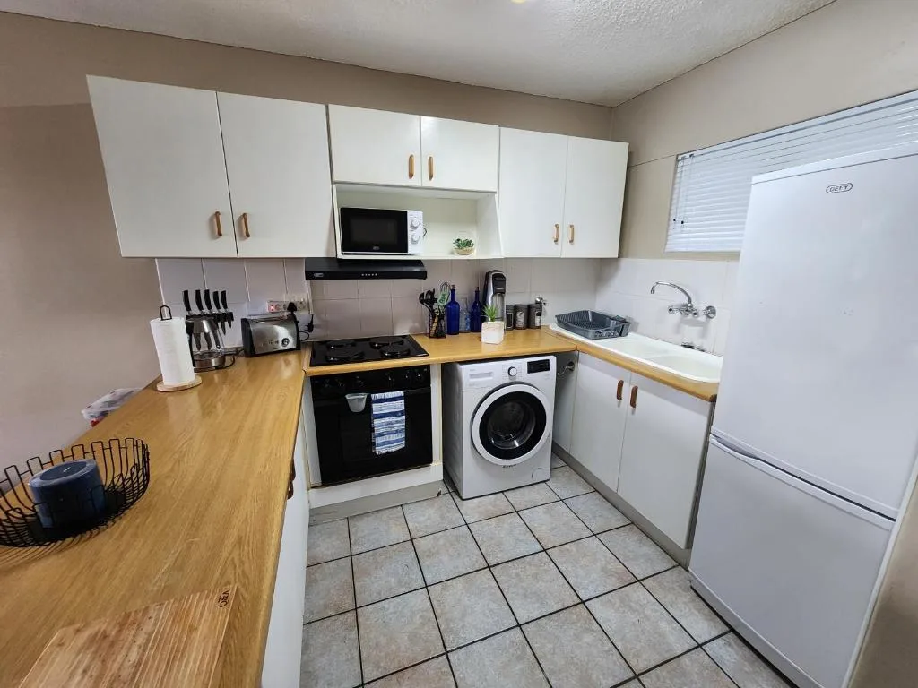Modern kitchen with white cabinetry, wooden counters, stove, washing machine, and appliances