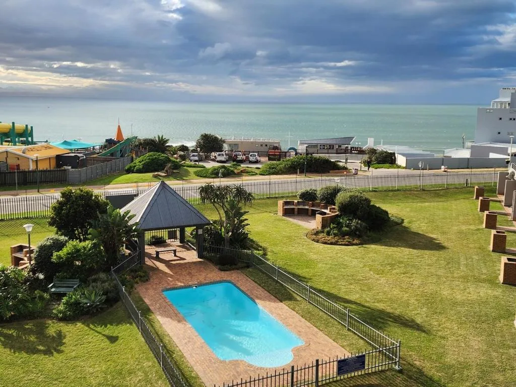 Blue swimming pool with gazebo and ocean view beyond manicured lawn