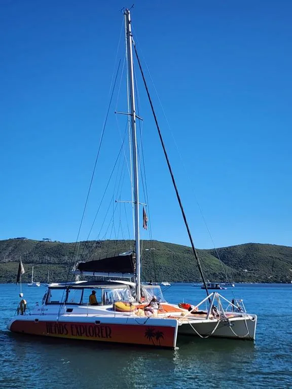 Sailboat anchored in pristine blue water with forested hills behind