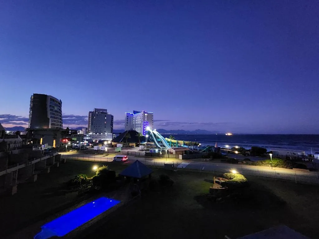 Twilight coastal view with illuminated beachfront buildings and glowing pool