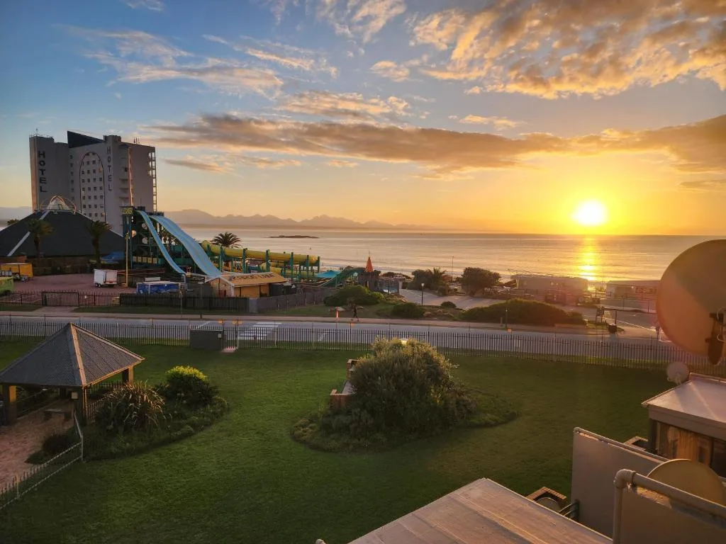 Golden sunset over ocean with manicured gardens and beachfront amusement park