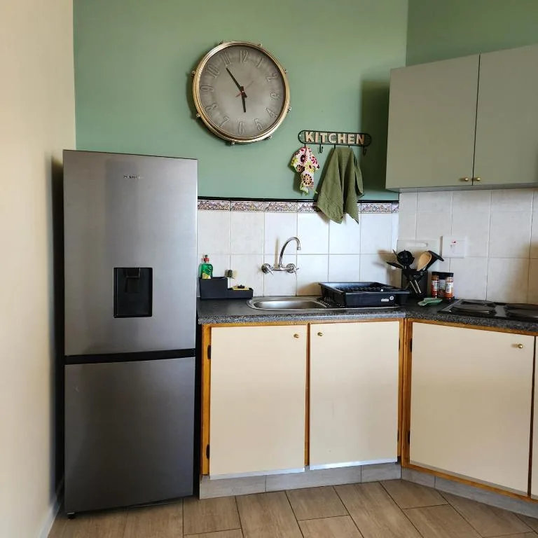 Compact kitchen with stainless steel fridge, white cabinetry, and wall clock